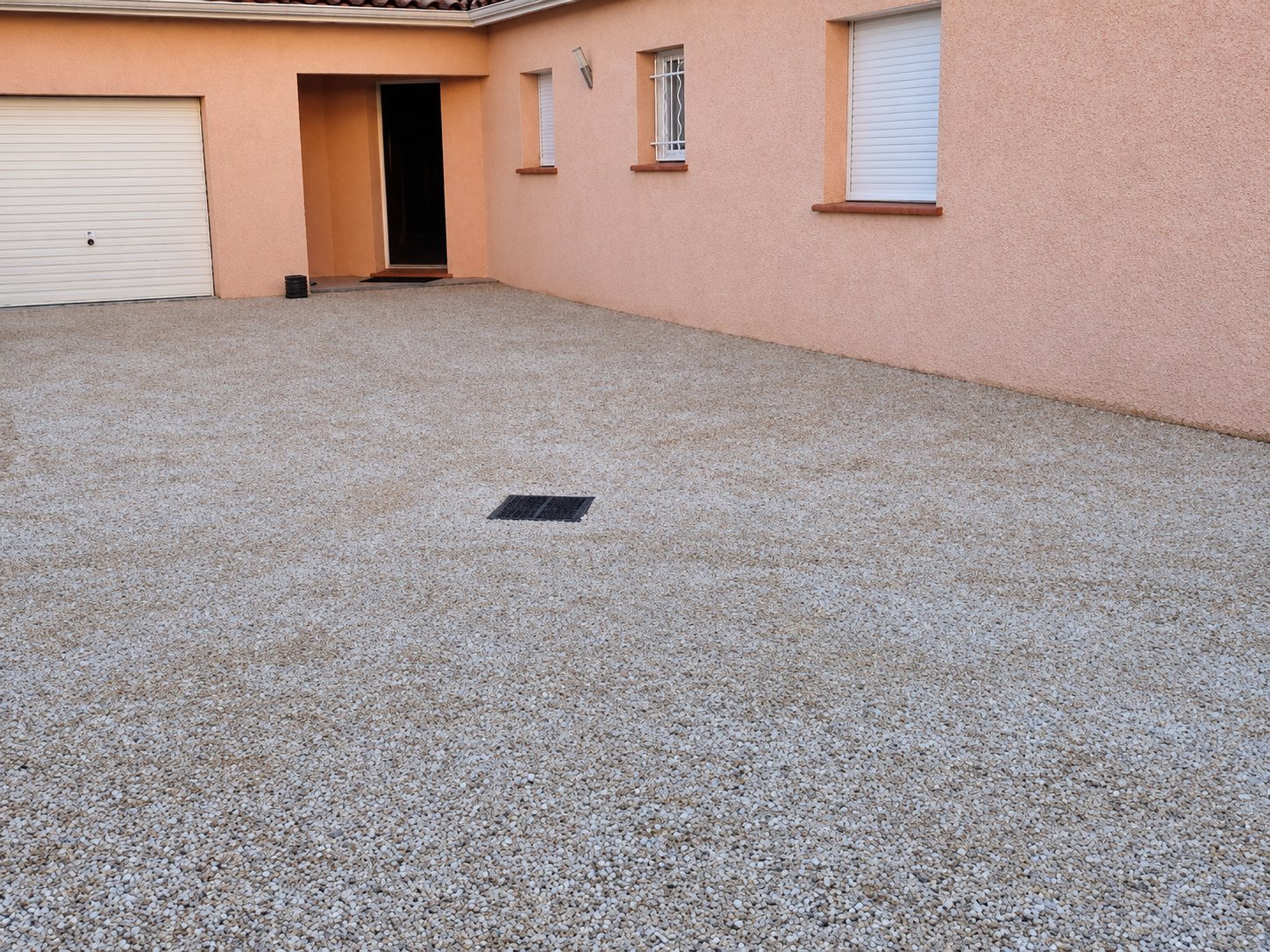 Cour gravillonnée devant une maison, avec le garage et l’entrée
