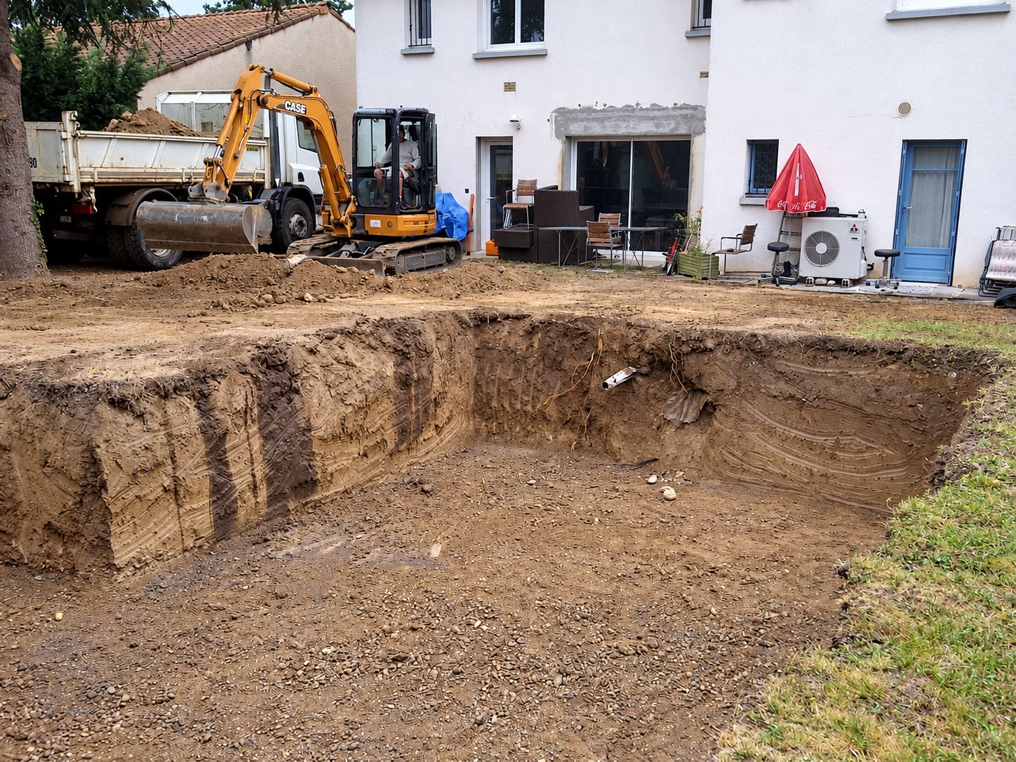 Mini-pelle et camion benne devant une maison, pendant le terrassement d’une piscine